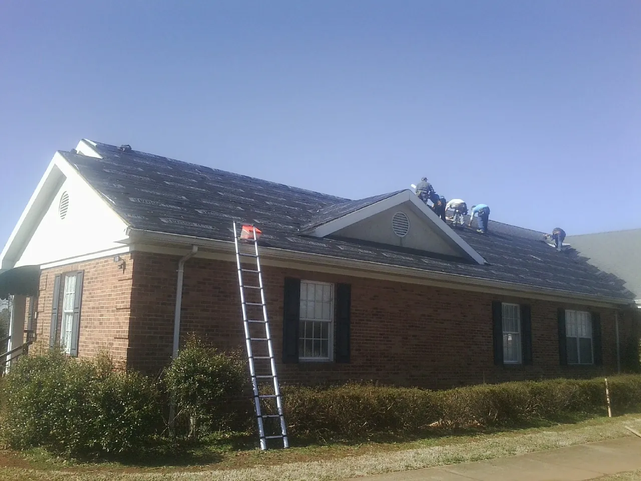 Crew tearing shingles off a brick ranch roof with a ladder set — Emergency Roof Repair work by our crew in Frankford