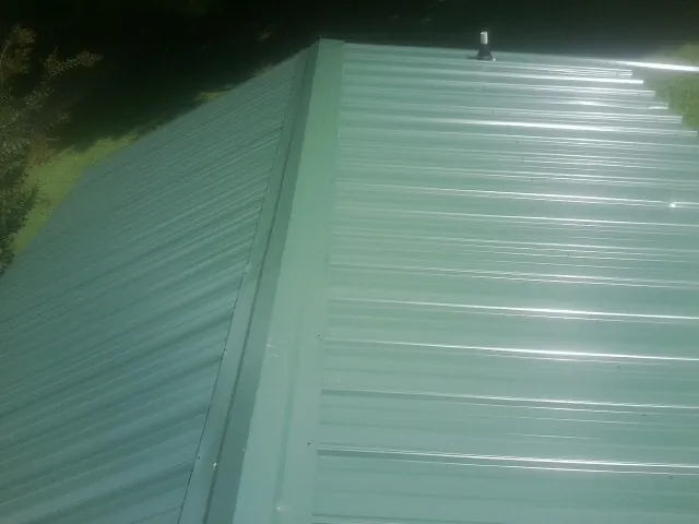 New green metal panels meeting at the ridge of a roof — Flat Roof Repair work by our crew in Frankford